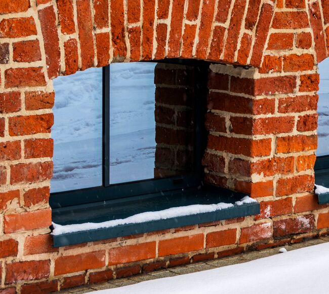 Dunkle, kleine Kellerfenster aus Aluminium in Ziegelmauer